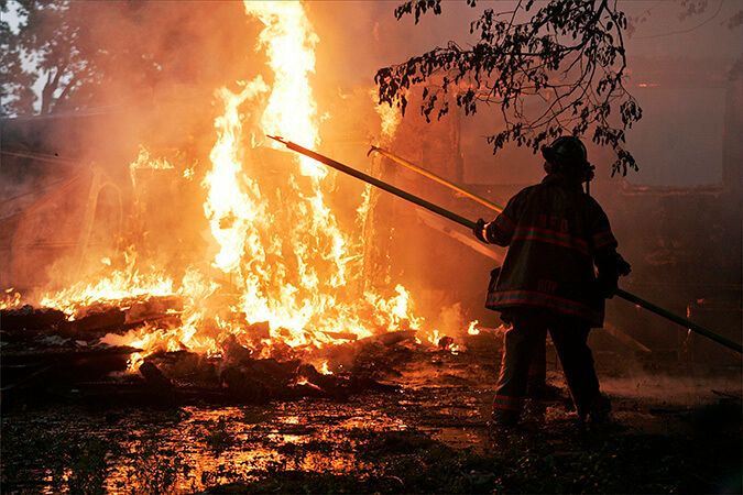 Firefighters Jon Klein and Ed Roy use pike poles to tear down a section of a burning home at 3315 Ridge Road in Highland,